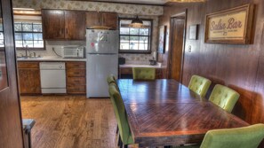 A kitchen with wooden cabinets, a refrigerator, a microwave, and a dining table with chairs. - Rock N Utopia (Utopia)