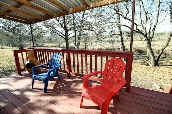 A wooden deck with two Adirondack chairs, one blue and one red, under a metal roof.