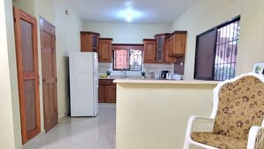 Un salón amplio con una cocina al fondo, un sofá blanco y suelo de baldosas.