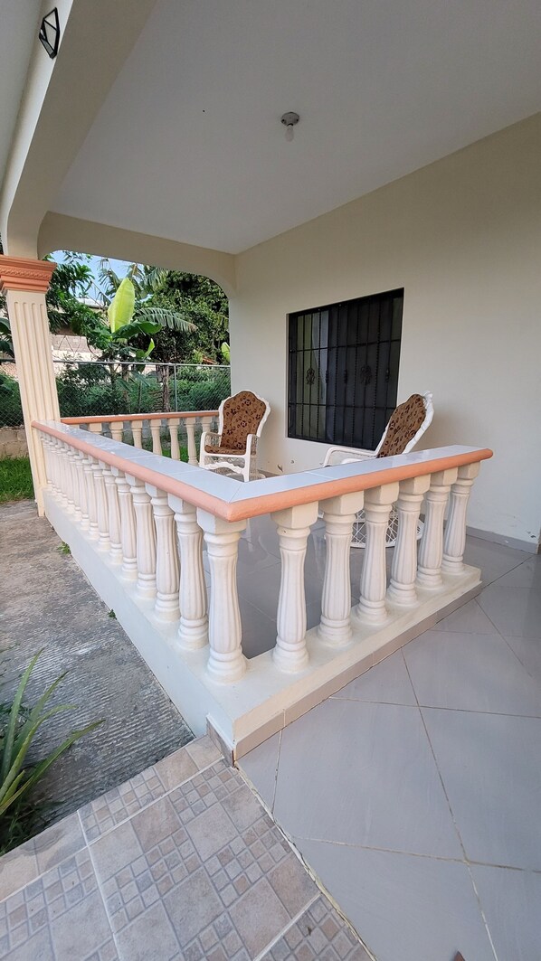 A covered outdoor seating area with a white balustrade and two chairs.