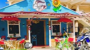 Un café con techo azul, mesas al aire libre y un letrero que dice 'Cafe'.