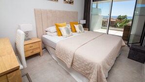 A bedroom with a large bed, a nightstand, a wooden desk, and a view of the sea through a large window. - Celere Dona Julia 2.3.0b (Casares)