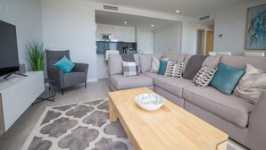 A modern living room with a grey sofa, a wooden coffee table, and a TV on a white cabinet. - Celere Dona Julia 2.3.0b (Casares)