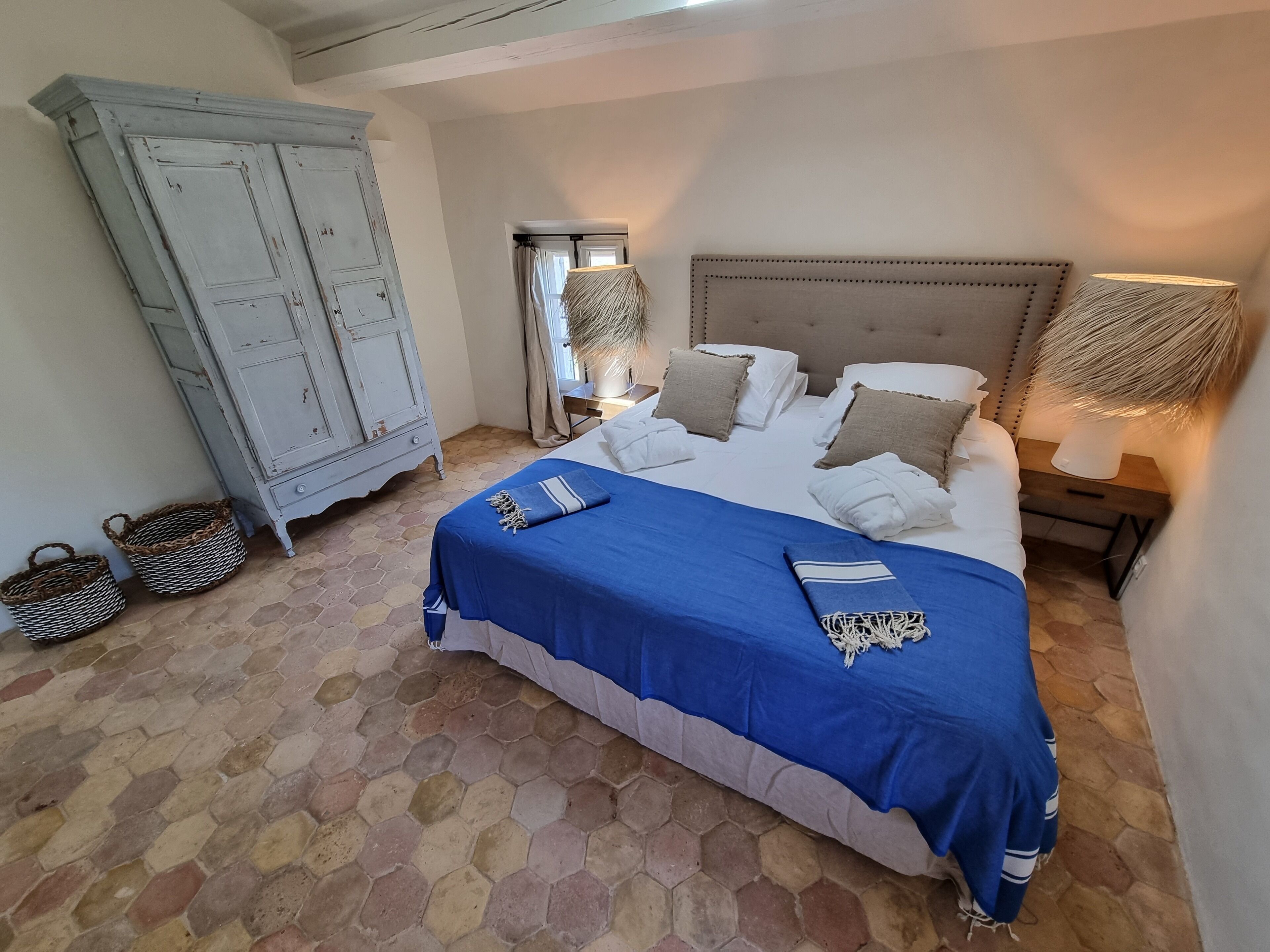 A bedroom with a large bed, a wardrobe, and a nightstand with a lamp.