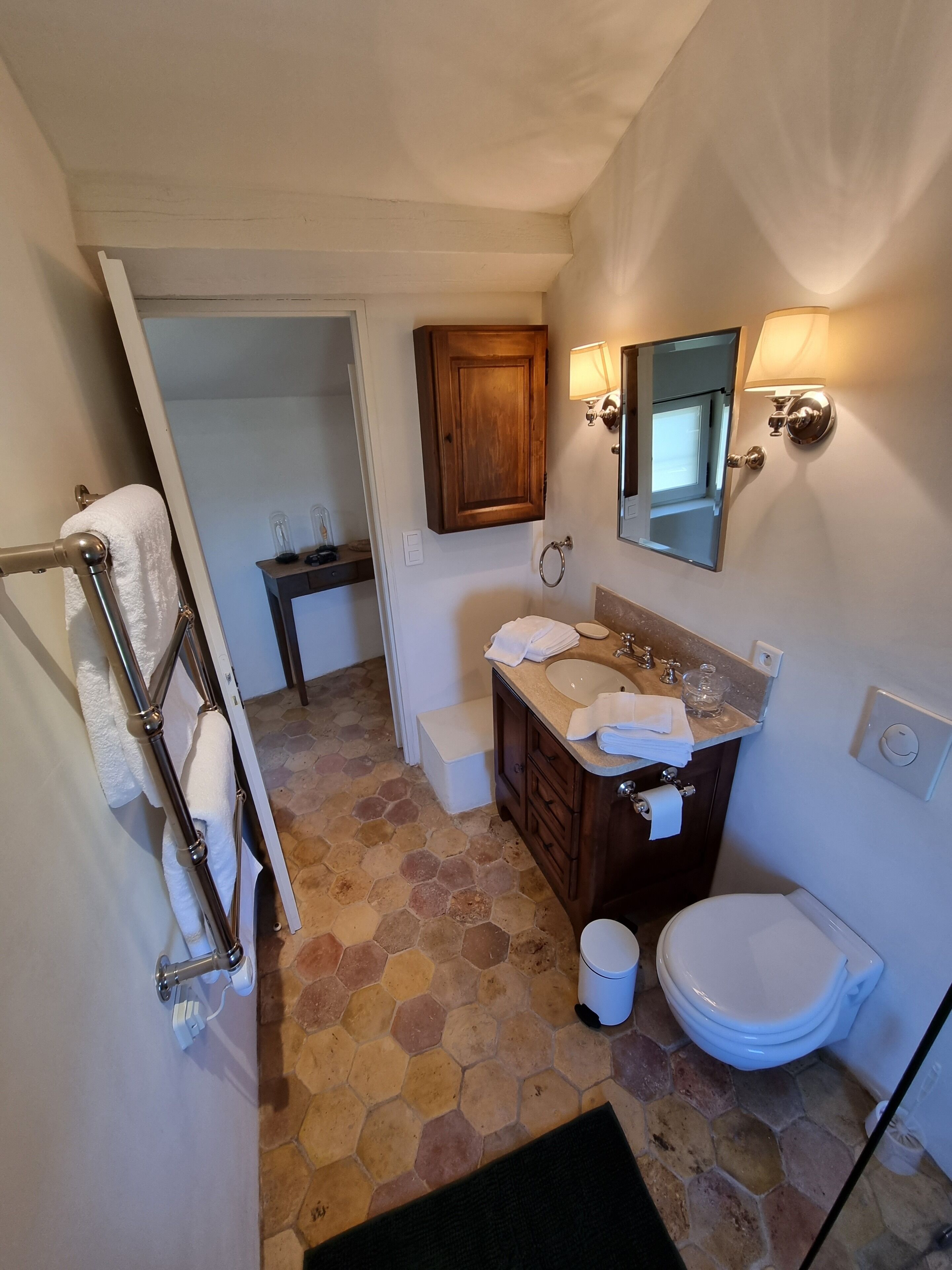 Une salle de bain avec un meuble-lavabo en bois, des toilettes, un lavabo avec un miroir et un porte-serviettes.