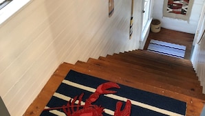 Un escalier avec un tapis représentant un crabe rouge au bas, des marches en bois et une fenêtre donnant sur l’extérieur.