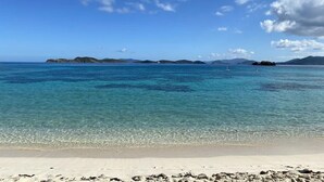 A beach with clear turquoise water, sandy shore, and distant islands.