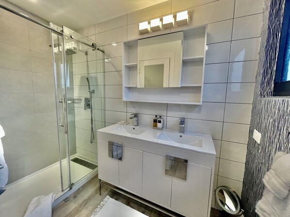 A modern bathroom with a glass shower enclosure, a white vanity with a sink, and a mirror above the vanity. - Sea Haven Villa - Renovated modern, 2-story, oceanfront at Sapphire Beach Resort (St Thomas)