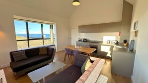 En modern inredning med en soffa, ett matbord, stolar och ett köksområde med utsikt över stranden.