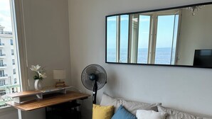 Een moderne woonkamer met een bank, een salontafel, een bureau met een ventilator en uitzicht op zee door grote ramen.