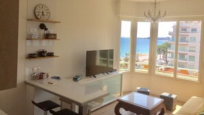 Een moderne woonkamer met een televisie, zitmeubels, een glazen tafel en uitzicht op zee.