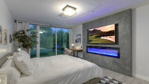 Een moderne slaapkamer met een groot bed, een televisie bevestigd aan een stenen muur en een schuifdeur naar een balkon.