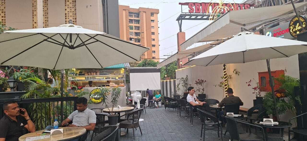 An outdoor café with tables and chairs, umbrellas, and potted plants.