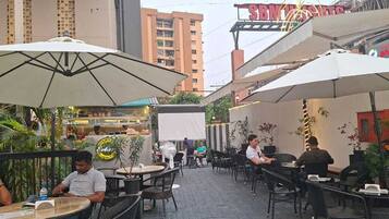 An outdoor café with tables and chairs, umbrellas, and potted plants.