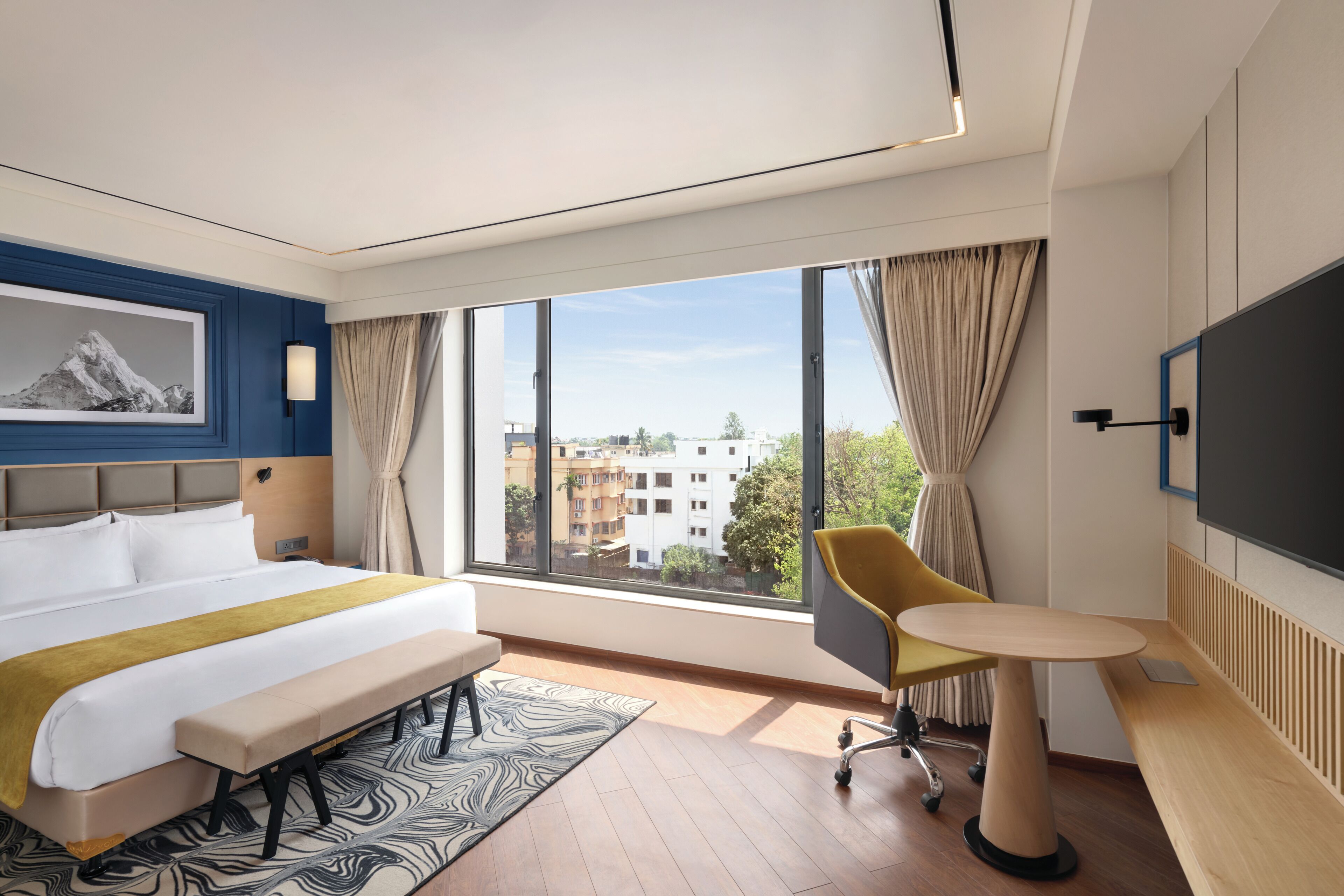 Habitació d'hotel moderna amb un llit gran, una taula de treball, una cadira i un televisor.