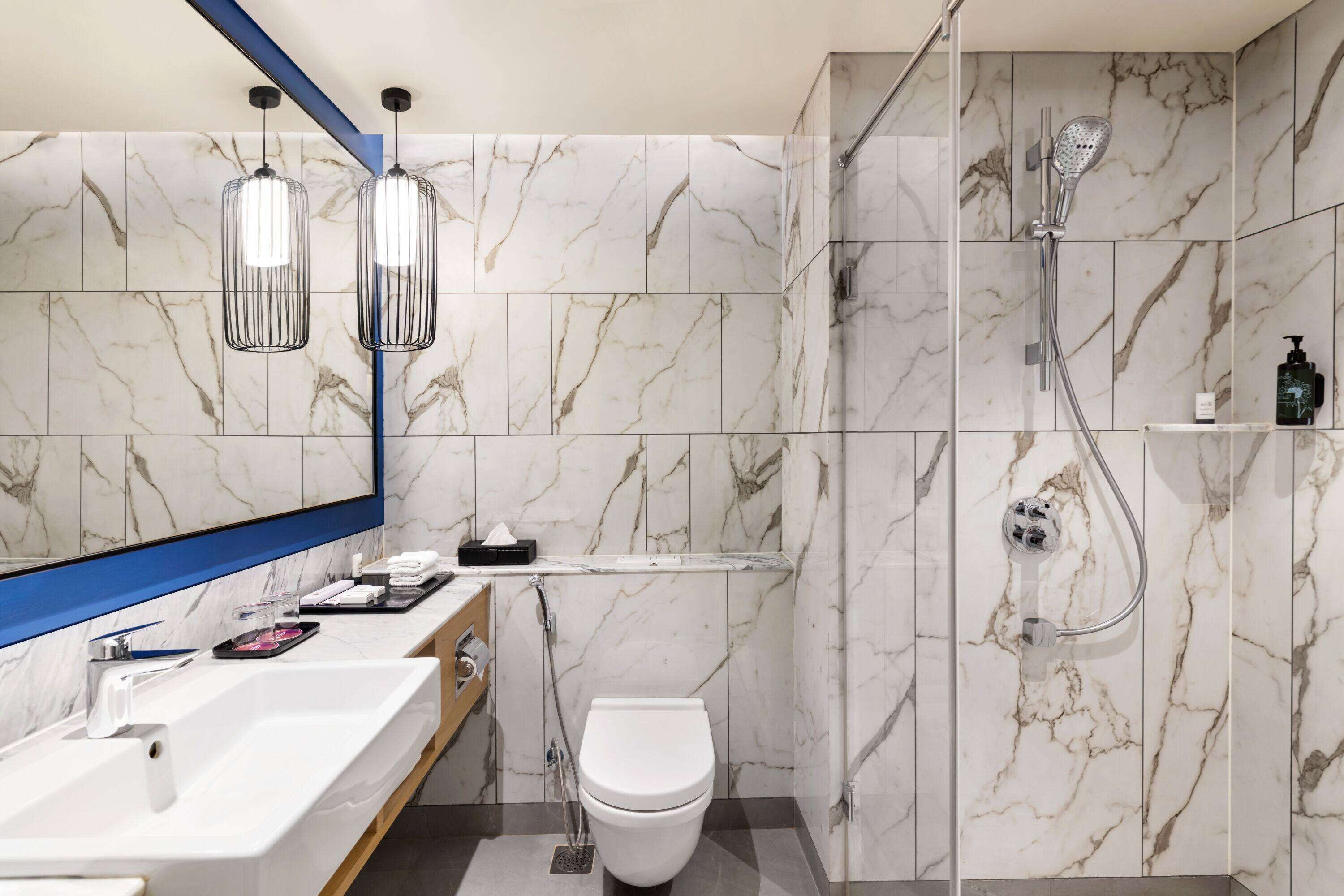 Un baño moderno con una salpicadera de mármol, un lavamanos blanco, un inodoro y una zona de ducha con mampara de vidrio.