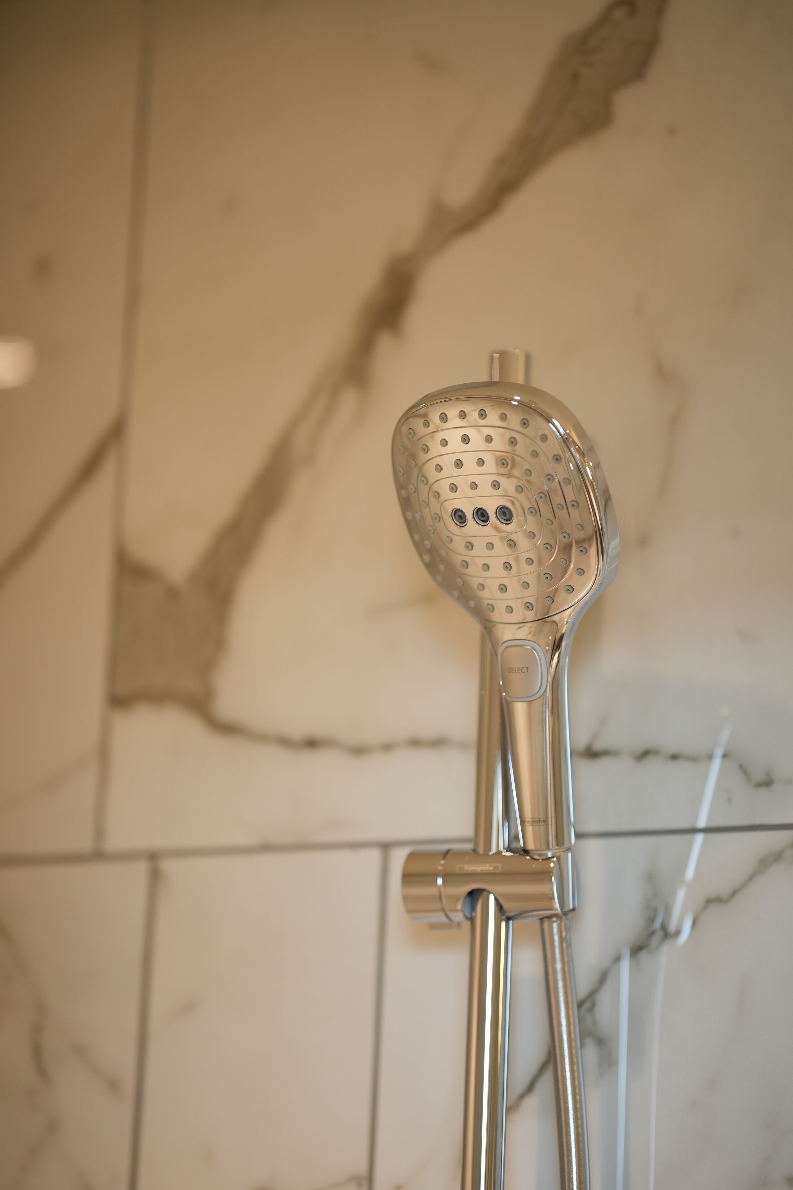Un cabezal de ducha con una perilla de control, fijado a una pared con diseño de mármol.