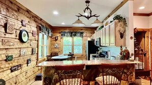 A rustic kitchen with wooden walls, a central island with bar stools, and a ceiling with a deer head light fixture. - "Deacon Escape", incredible and quiet getaway. (Newland)