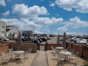 A coastal parking area with multiple cars, a building with a blue facade, and a view of the sea and boats in the distance. - Coast View Apartment (Lyme Regis)