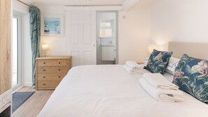 A bedroom with a bed, bedside tables, a dresser, a chandelier, and a door leading to a bathroom. - Coast View Apartment (Lyme Regis)