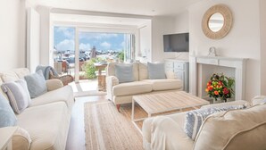 A spacious living room with a sofa set, a coffee table, a fireplace, a TV, and a view of the marina. - Coast View Apartment (Lyme Regis)