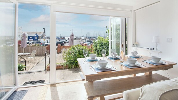 A dining area with a view of a marina, a wooden table set for two, and a glass door leading to an outdoor patio. - Coast View Apartment (Lyme Regis)