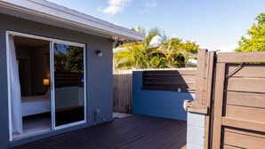 Una terraza de madera con un ventanal corredero que da a una habitación con una cama.