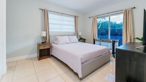 Un dormitorio con cama, mesitas de noche, cómoda y ventana con cortinas.