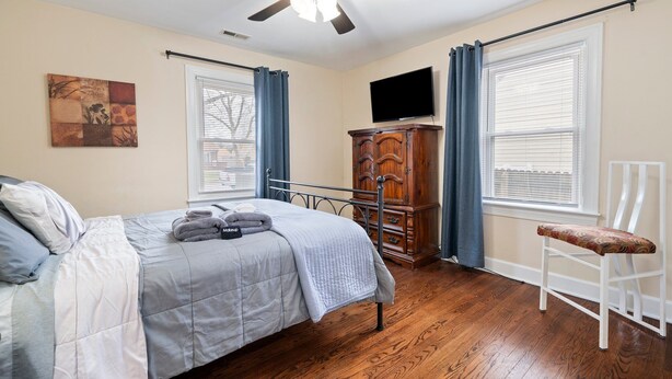 A bedroom with a bed, a ceiling fan, a dresser, a TV, and a chair.