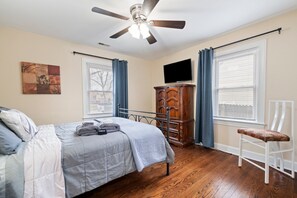 Ein Schlafzimmer mit Bett, Deckenventilator, Kommode, Fernseher und Stuhl.