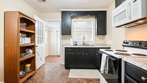 A kitchen with a wooden pantry, black cabinets, a white stove, and a microwave.