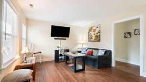 A living room with hardwood flooring, a flat-screen TV, a sofa, a coffee table, and a lamp.