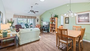 A spacious living room with a sofa, chairs, a dining table, and a TV. - Close to Pelican Heron Golf Course and only  7 minutes to Lake Sumter Landing (The Villages)