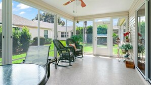 A sunroom with a ceiling fan, large sliding glass doors, a glass table, and wicker chairs. - Close to Pelican Heron Golf Course and only  7 minutes to Lake Sumter Landing (The Villages)