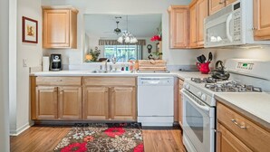 A modern kitchen with wooden cabinets, a built-in dishwasher, a stove, and a microwave. - Close to Pelican Heron Golf Course and only  7 minutes to Lake Sumter Landing (The Villages)