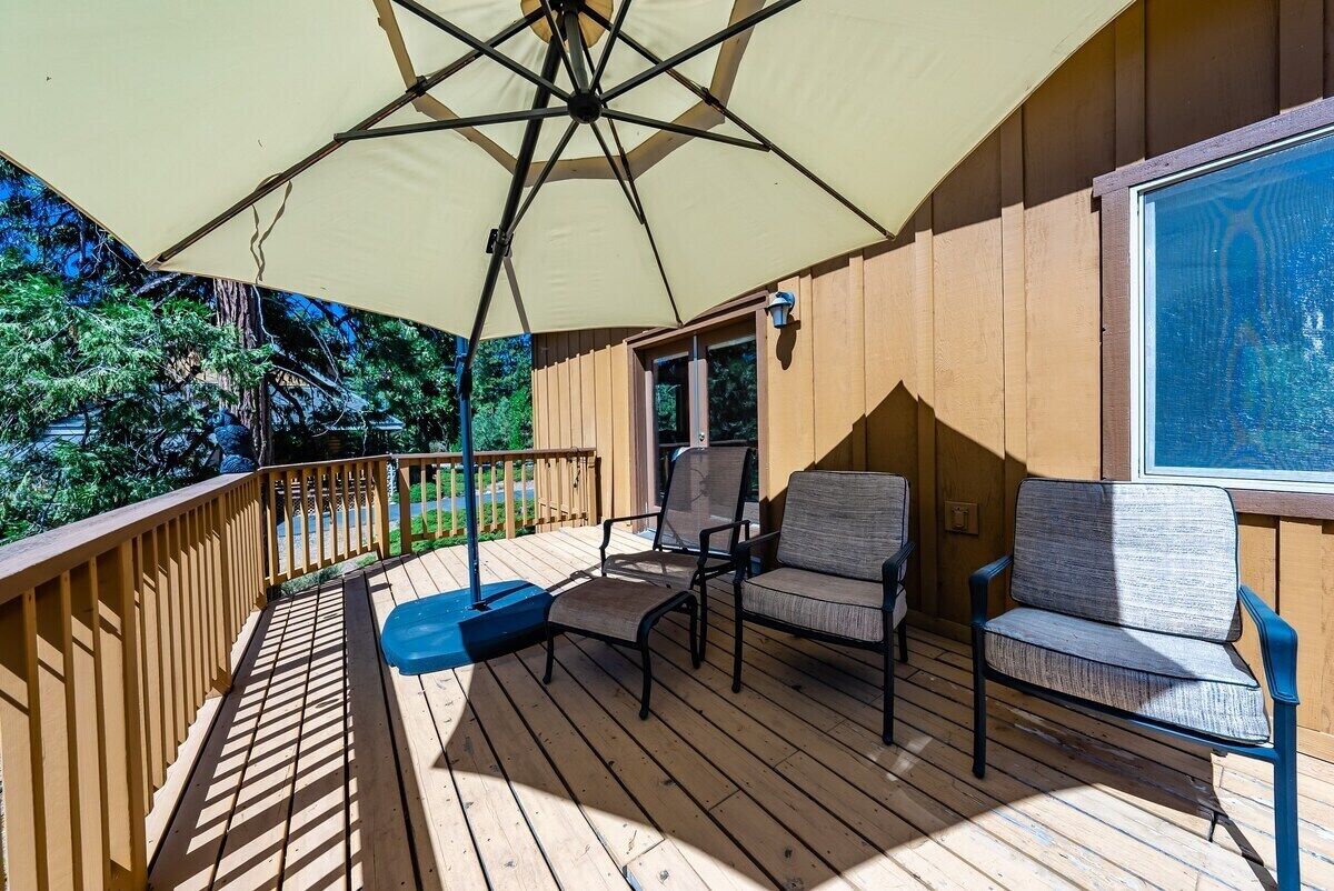 Une terrasse en bois avec une chaise suspendue, un fauteuil rembourré et un grand parasol pour faire de l’ombre.