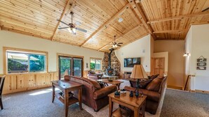 A spacious living room with a high wooden ceiling, a fireplace, and a television. - The Restful Rose ~ Fireside Vibes + AC Comfort (Shaver Lake)