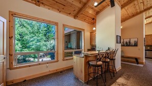 A spacious kitchen with large windows, wooden ceiling, and a bar area with chairs. - The Restful Rose ~ Fireside Vibes + AC Comfort (Shaver Lake)