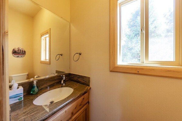 A bathroom with a wooden vanity, a white sink, a large mirror, and a window with a view of trees.