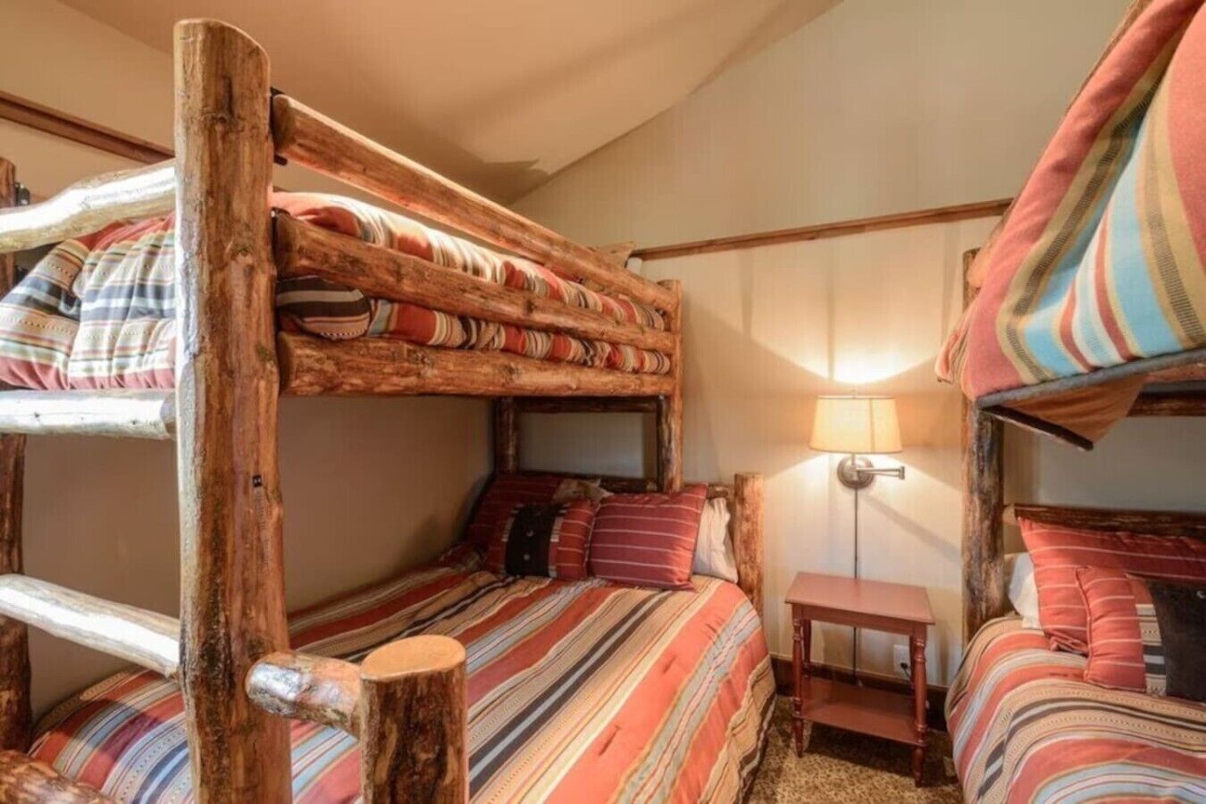 A rustic room with bunk beds, striped bedding, a small bedside table, and a lamp.