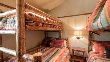 A rustic room with bunk beds, striped bedding, a small bedside table, and a lamp.