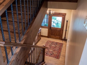 A wooden staircase leading to a room with a door, a chandelier, and a rug.
