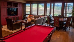 Una mesa de billar en una habitación con un ventanal grande, un sofá y una televisión.