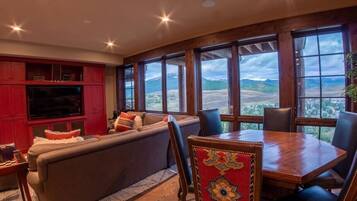 A room with a large window, a sofa, a dining table, and a red cabinet.