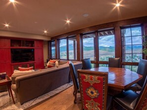 A room with a large window, a sofa, a dining table, and a red cabinet.