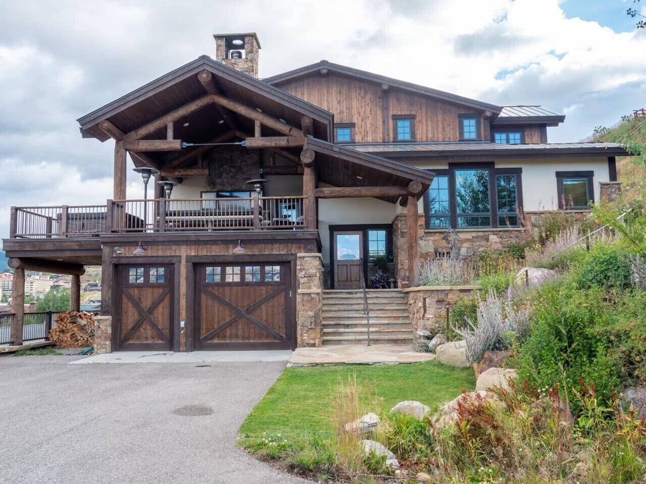 A two-story house with a balcony, large garage doors, and a stone chimney.