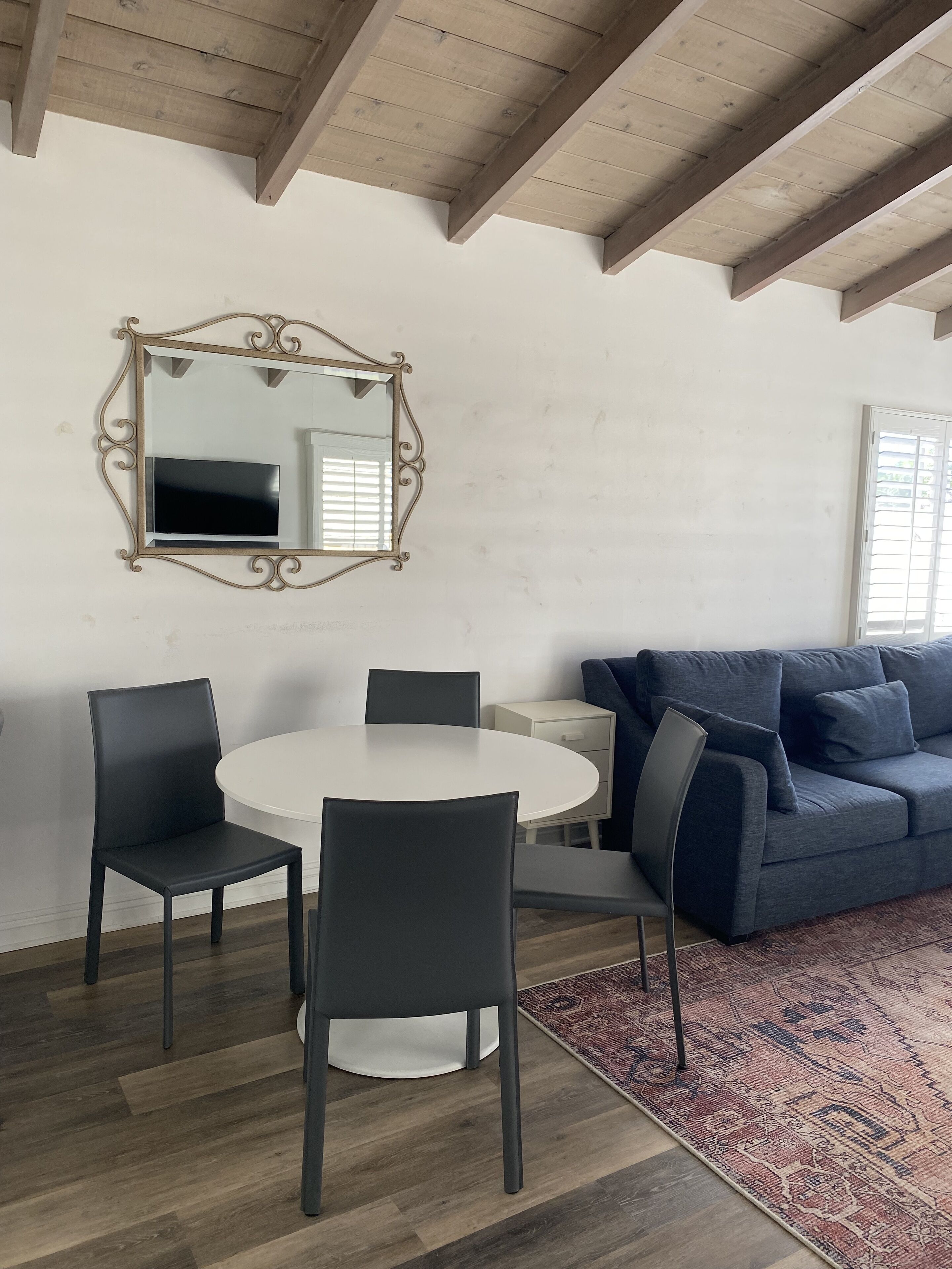 Ein Zimmer mit einem runden weißen Tisch, vier Stühlen, einem blauen Sofa, einem gemusterten Teppich und einem Spiegel mit aufwendigem Rahmen.