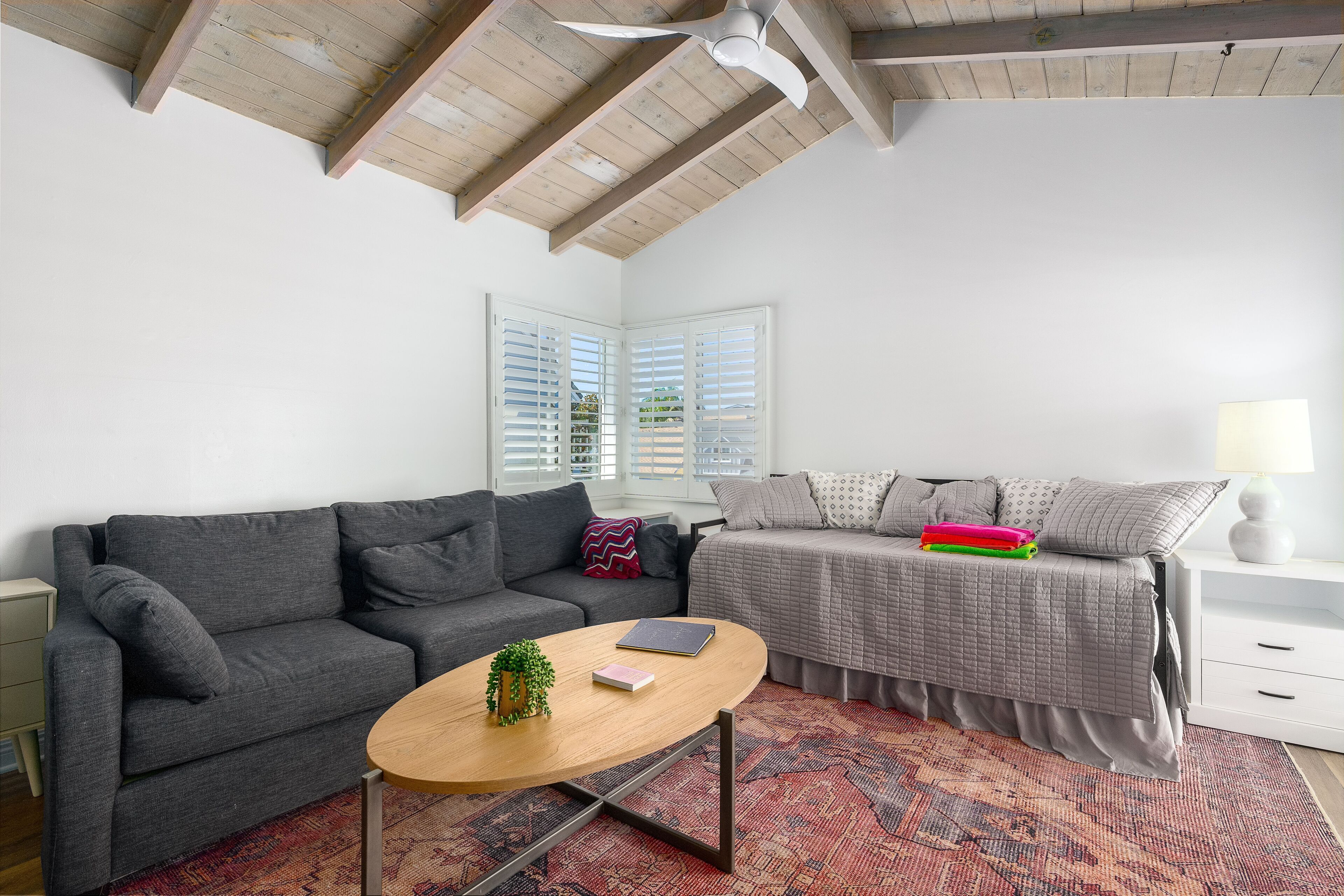 A modern bedroom with a grey sofa, a bed with a grey duvet, a small wooden coffee table, and a patterned rug.