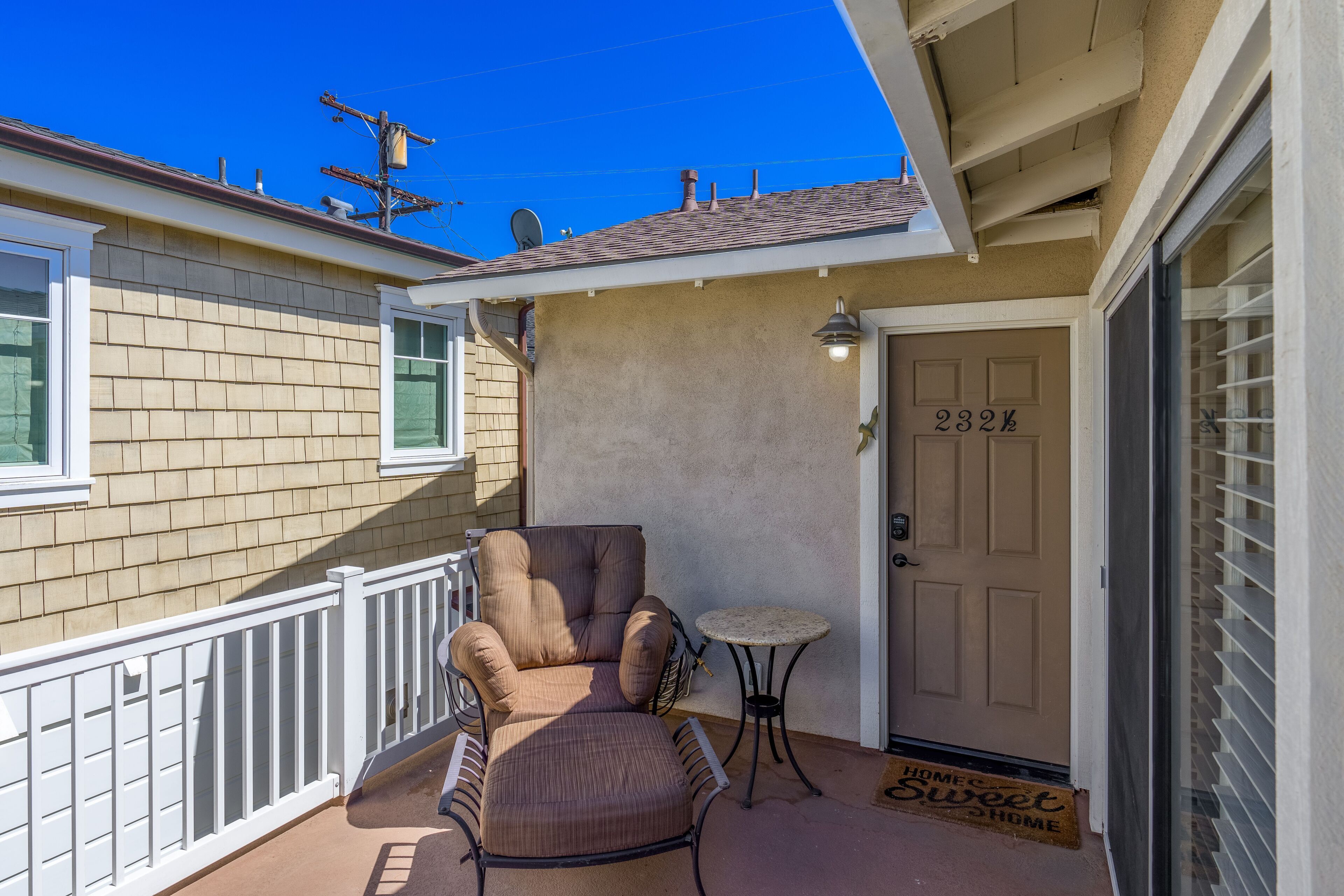 A covered porch with a cushioned chair, a small table, and a door marked "232".