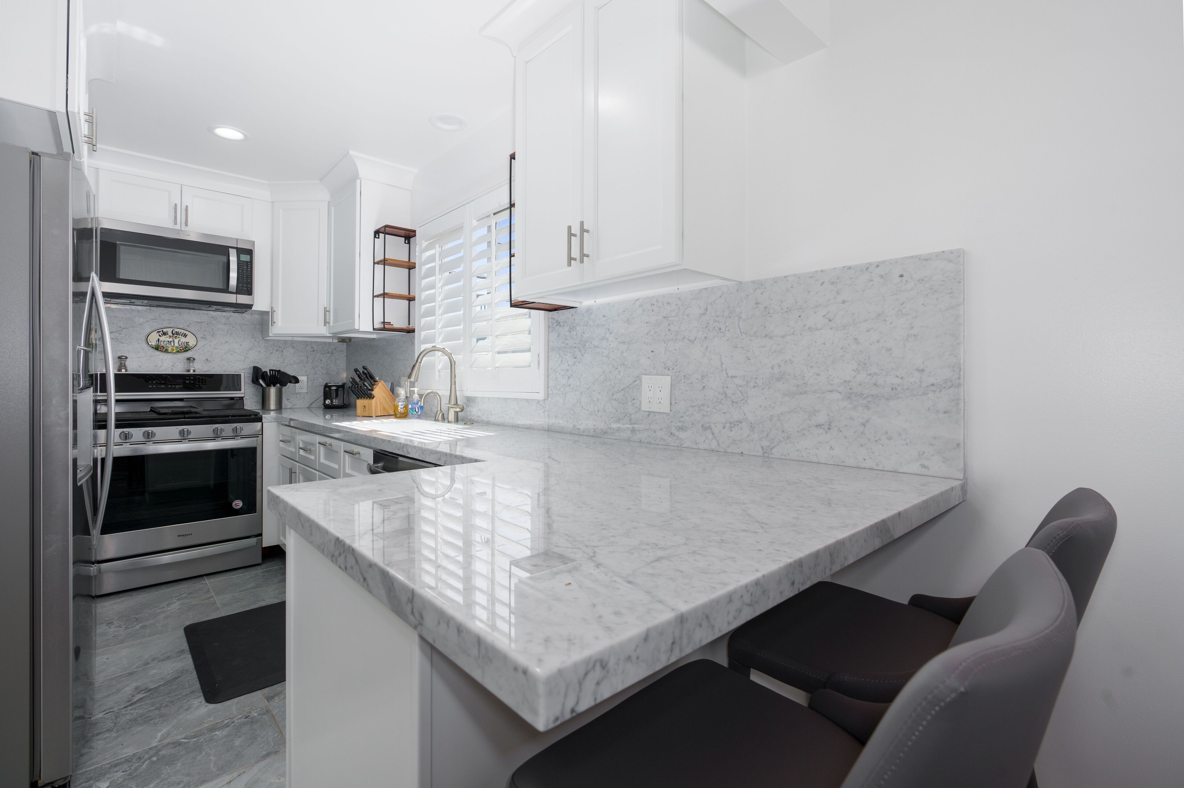 A modern kitchen with white cabinetry, a marble countertop, stainless steel appliances, and a built-in oven.